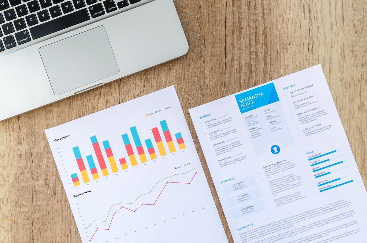 Two printed documents, one with bar and line charts, beside a laptop on a wooden desk